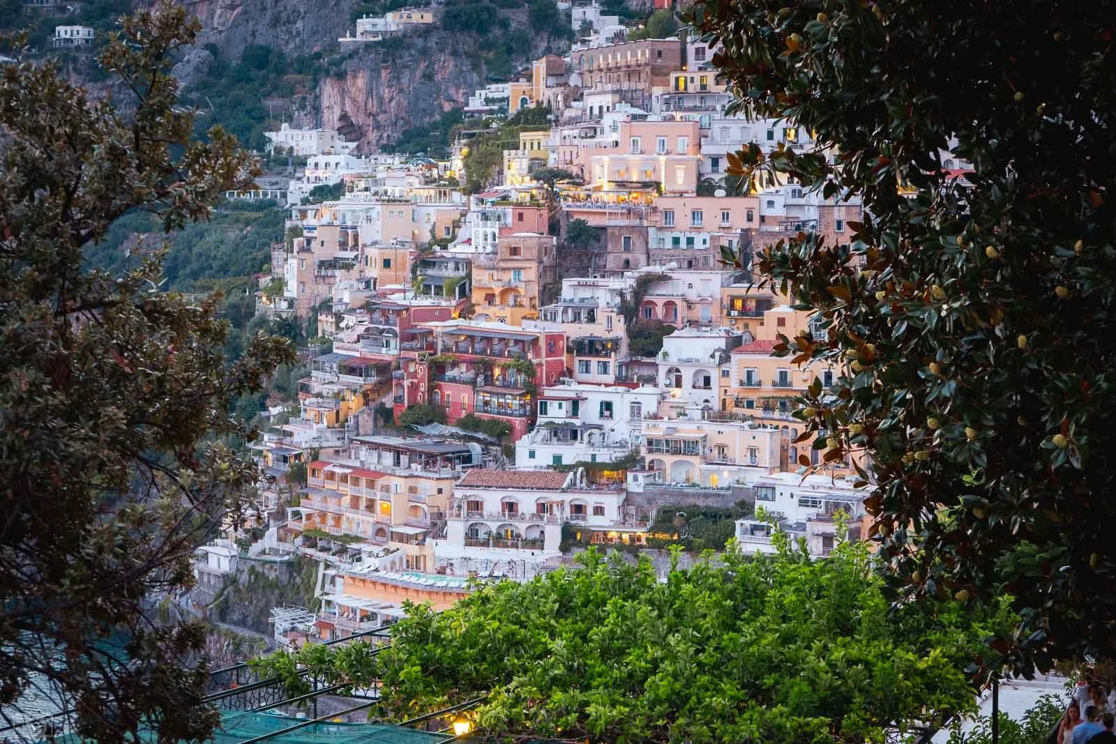 Village coloré construit en terrasses sur une colline avec des arbres verts en premier plan.