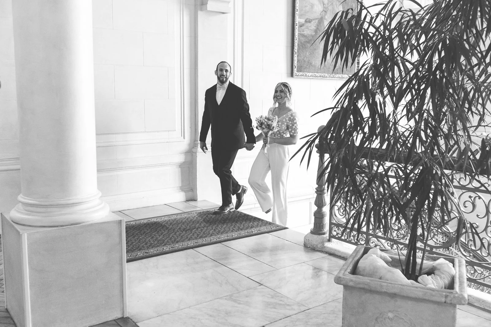 Un couple souriant, la femme tenant un bouquet, se tenant main dans la main dans un intérieur élégant.