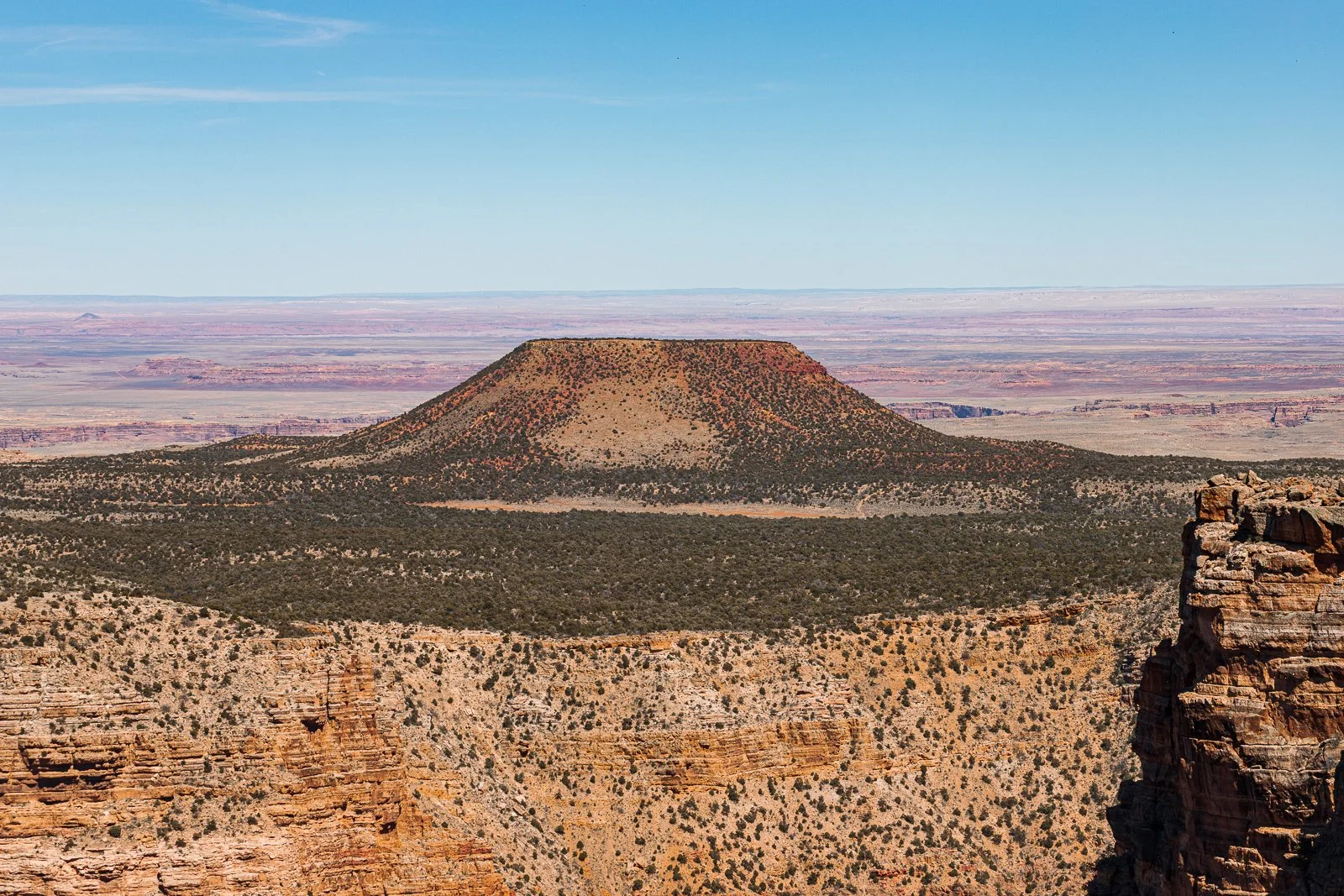 Une formation rocheuse massive dans un paysage désertique avec peu de végétation, sous un ciel bleu clair.