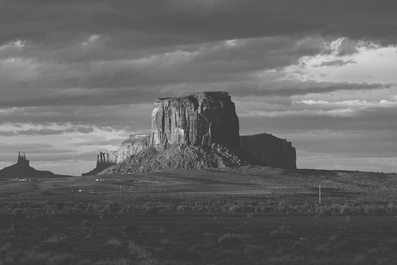 Une formation rocheuse massive au milieu d'une plaine, sous un ciel nuageux, en noir et blanc.