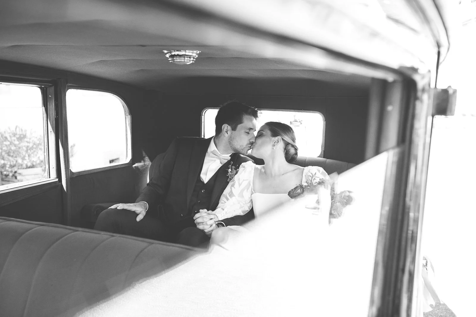 Un couple marié partage un baiser dans l'intérieur d'une ancienne voiture.