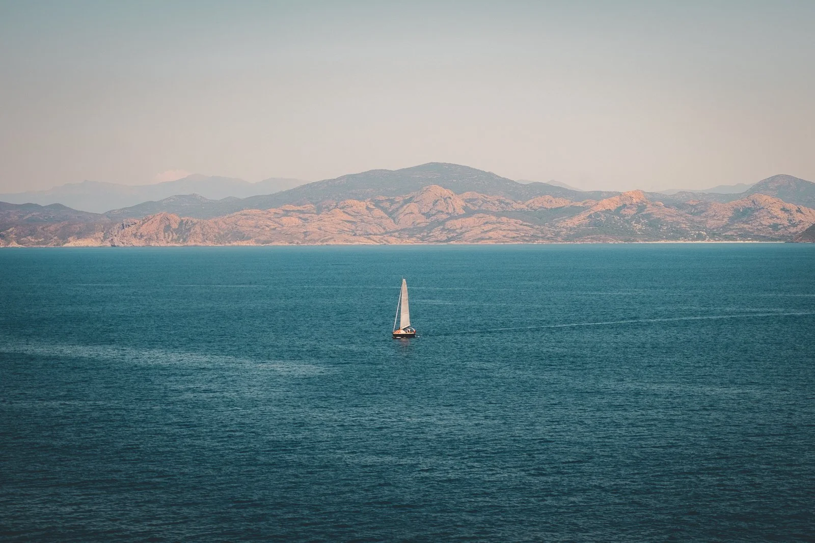 Un voilier naviguant sur une mer calme avec une chaîne de montagnes en arrière-plan.