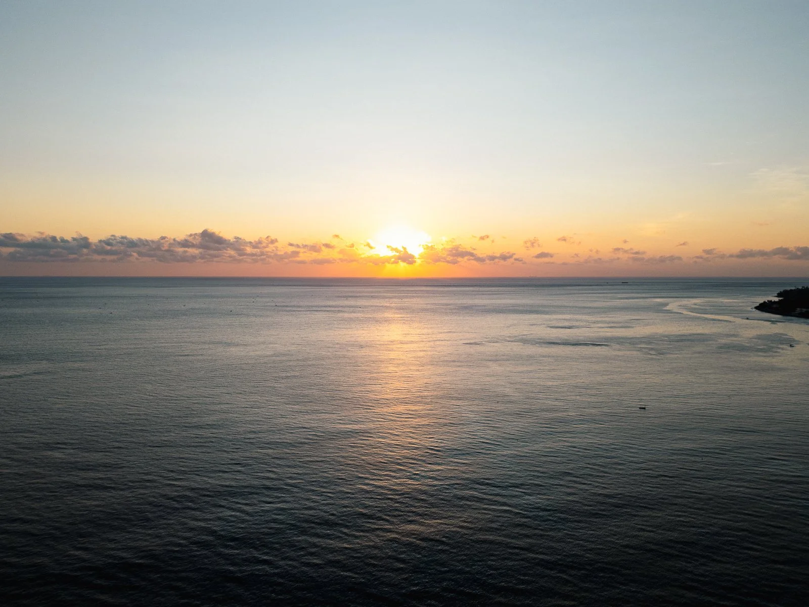 Coucher de soleil sur la mer, avec des nuages dispersés et des reflets dorés sur l'eau.