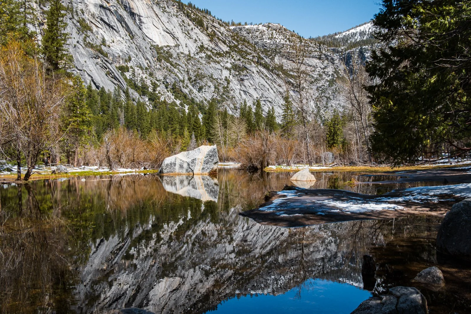 Un lac calmes entouré d'arbres et de montagnes rocheuses en arrière-plan, avec des reflets parfaits du paysage dans l'eau.