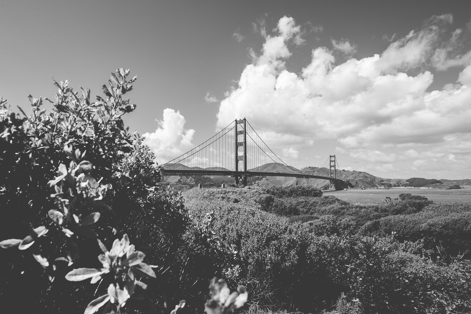 Photo en noir et blanc du pont du Golden Gate avec des collines en arrière-plan et des nuages dans le ciel.