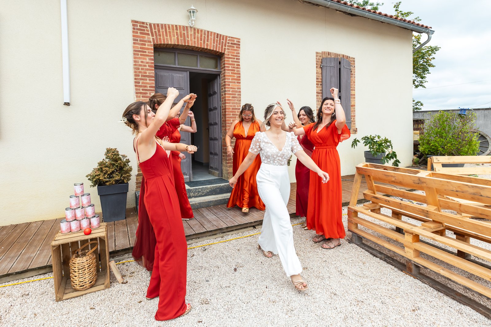 Groupe de femmes célébrant dehors, une femme en blanc danse au centre, entourée de femmes en robes rouges, dans une ambiance joyeuse