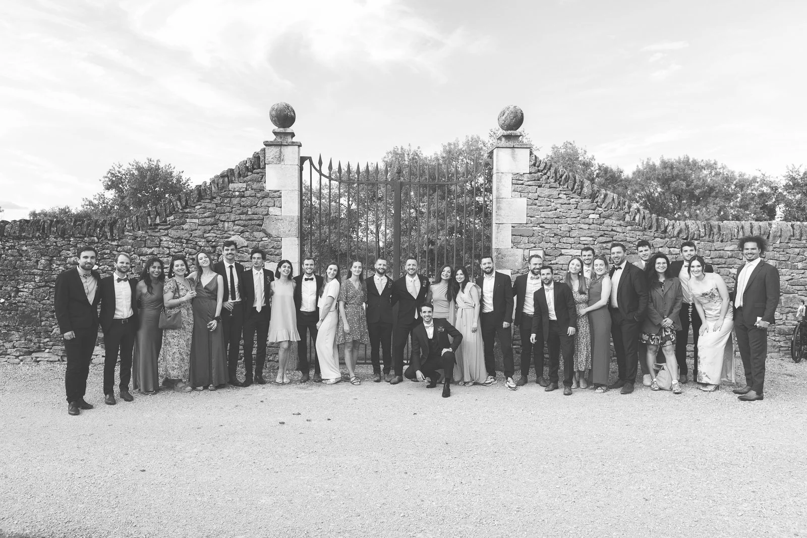 groupe de personnes habillées en tenues formelles posant devant une porte en pierre dans un cadre extérieur.
