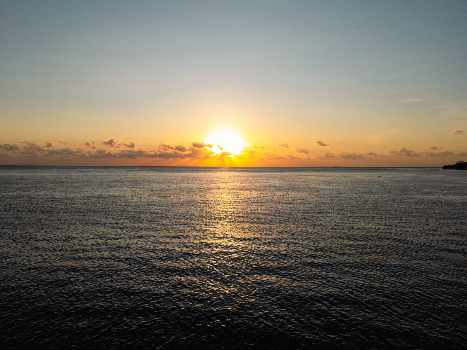 Lever de soleil sur la mer, avec le ciel clair et quelques nuages à l'horizon.