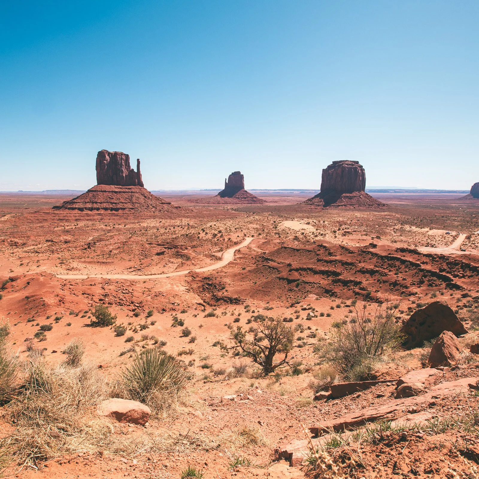 Paysage désertique avec des formations rocheuses appelées buttes ou mesas, sous un ciel clair et bleu.