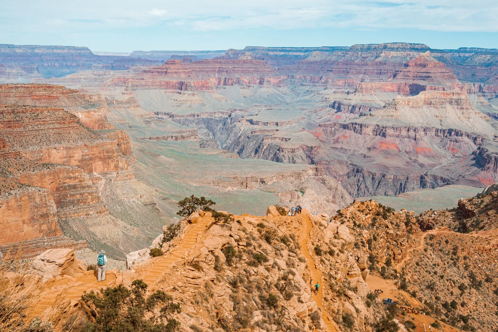 Vue panoramique du Grand Canyon avec des sentiers de randonnée, quelques touristes explorant, et la géographie rocheuse multicolore des falaises et des gorges.