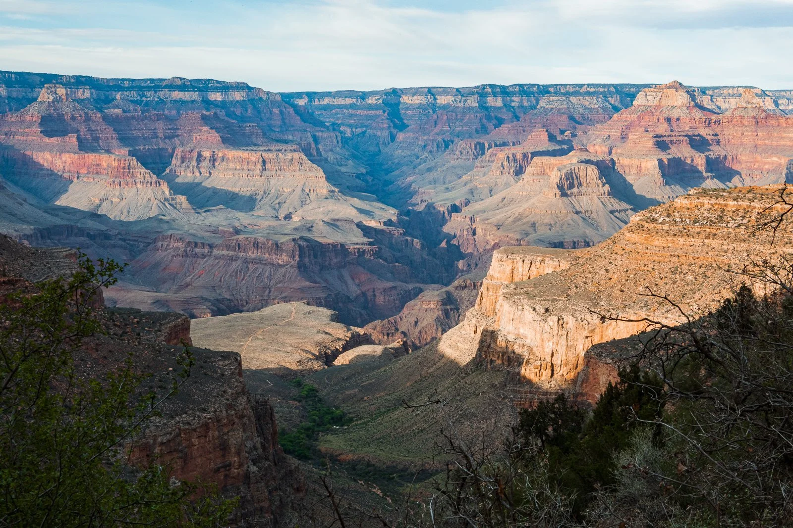 Vue panoramique du Grand Canyon avec ses formations rocheuses colorées et le fond sous un ciel clair.