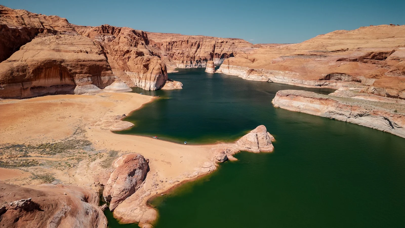 Vue aérienne d'un lac au fond d'une gorge rocheuse, avec des murs de canyon en sandstone, sous un ciel clair.