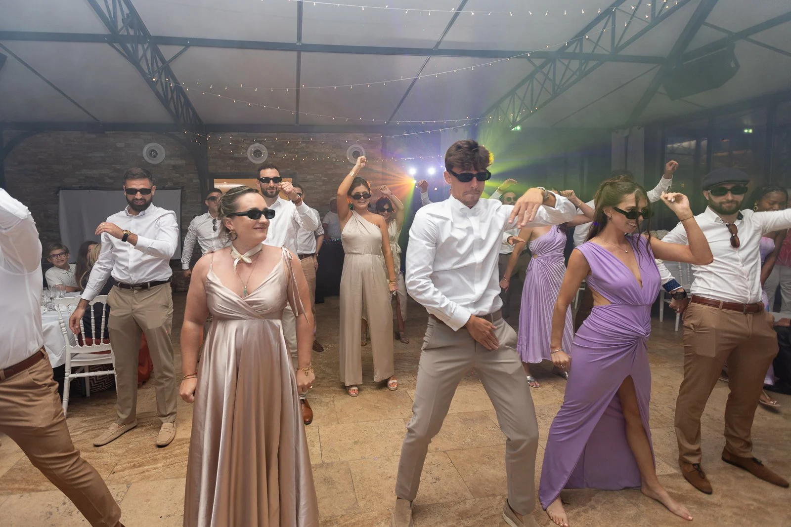 Groupe de personnes en tenue élégante dansant lors d'une fête ou d'un événement, avec des lumières colorées et une ambiance festive.