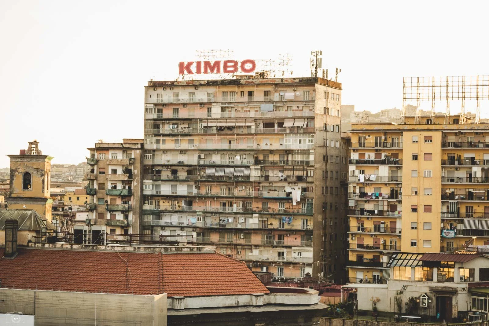 Vue urbaine de plusieurs immeubles résidentiels avec un grand panneau publicitaire 'KIMBO' sur le toit de l'immeuble central
