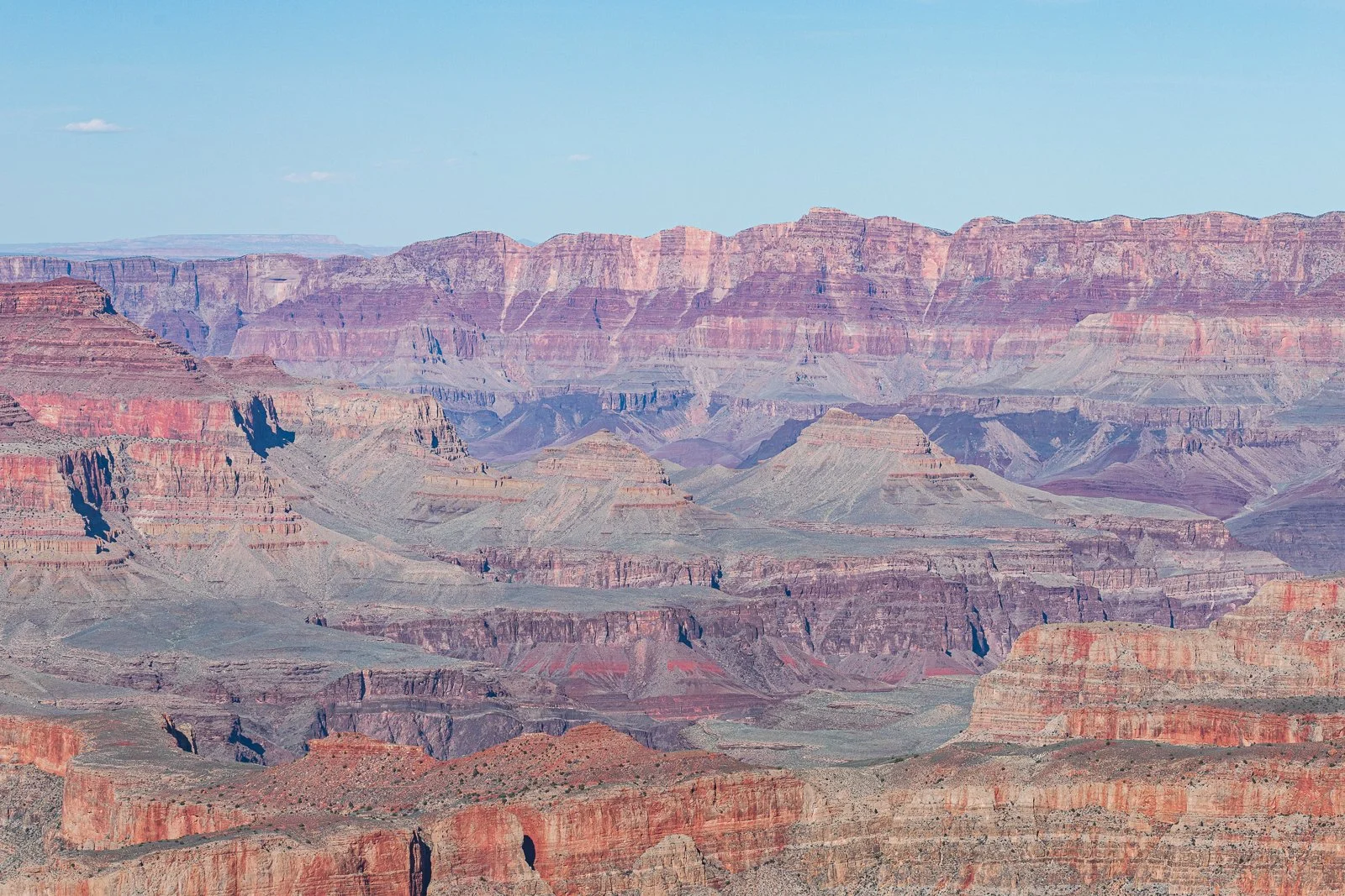 Vue du Grand Canyon avec ses roches stratifiées en différentes couleurs, sous un ciel clair.