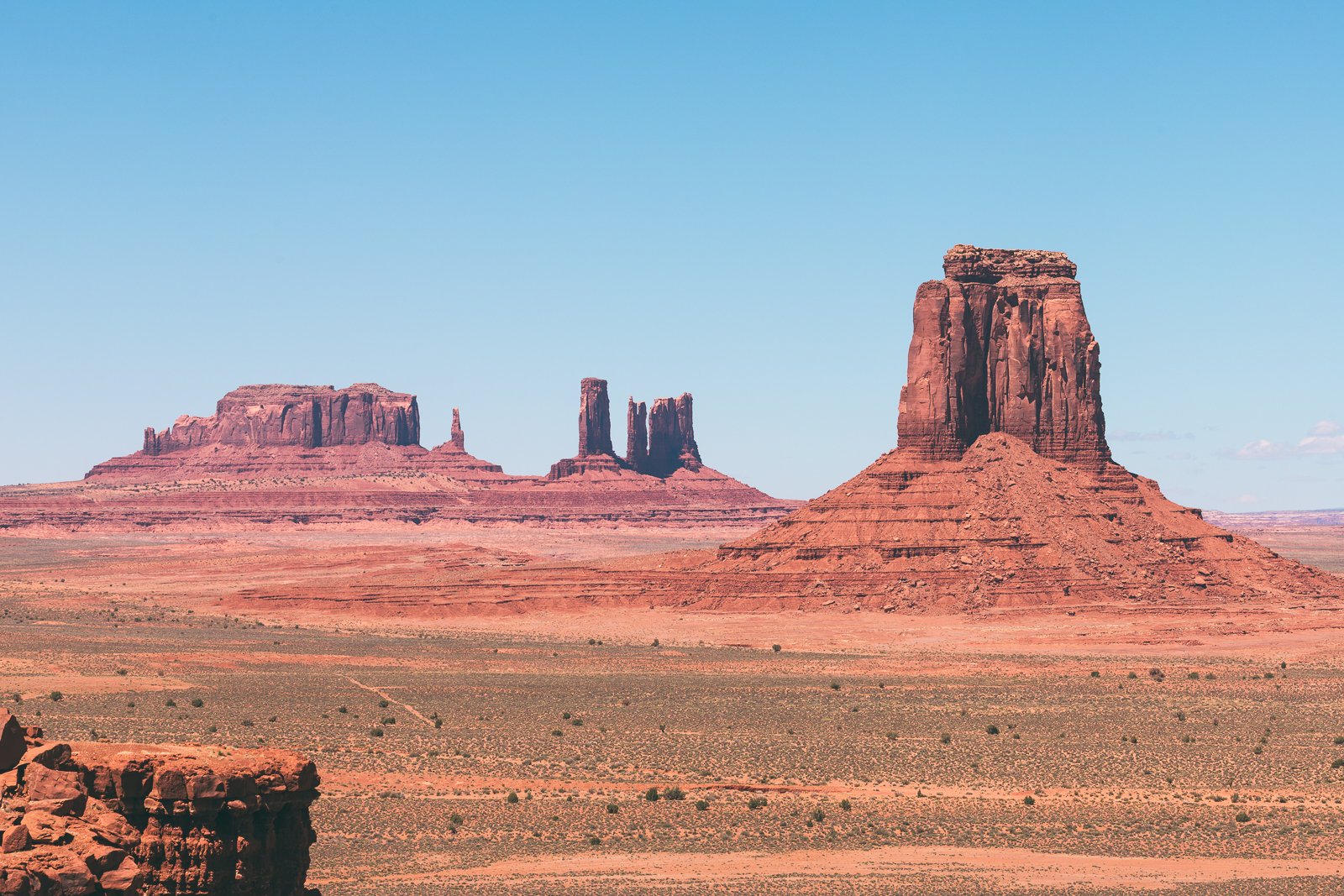 Paysage désertique avec de grandes formations rocheuses rouges sous un ciel bleu clair.