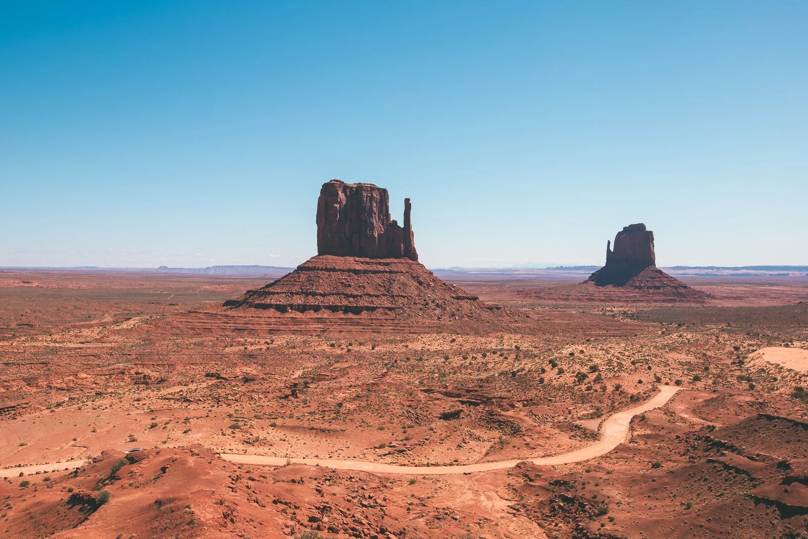 Paysage désertique avec deux formations rocheuses monumentales dans la région de Monument Valley, sous un ciel bleu clair.
