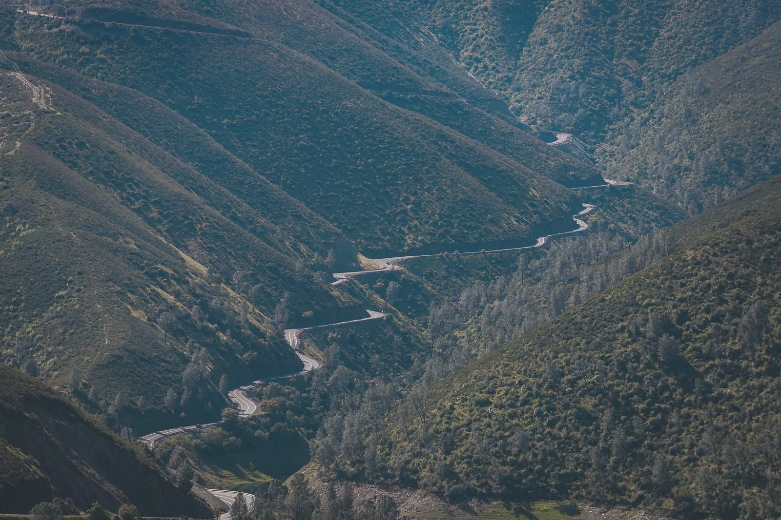 Une route sinueuse traverse une vallée entourée de montagnes verdoyantes.