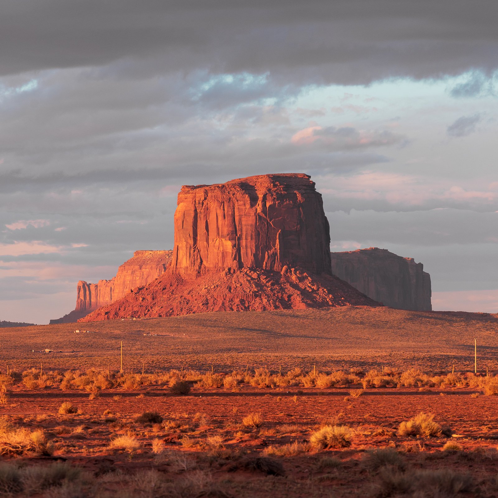 Un célèbre monument rocheux dans le désert, probablement le Devil's Tower, éclairé par la lumière du coucher de soleil avec un ciel partiellement nuageux.