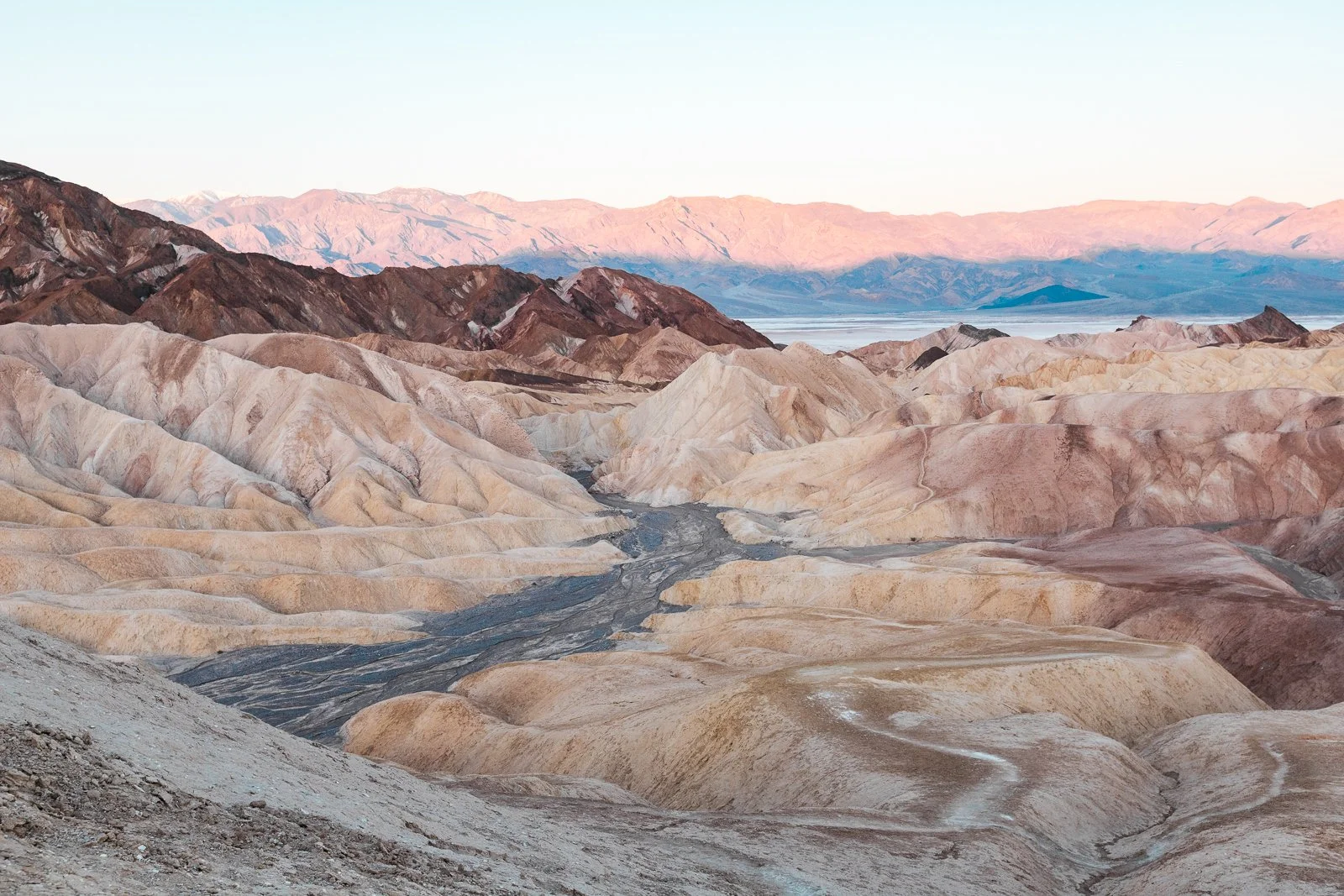 Paysage désertique avec des montagnes colorées et des formations rocheuses, ciel clair, à l'aube ou au crépuscule.