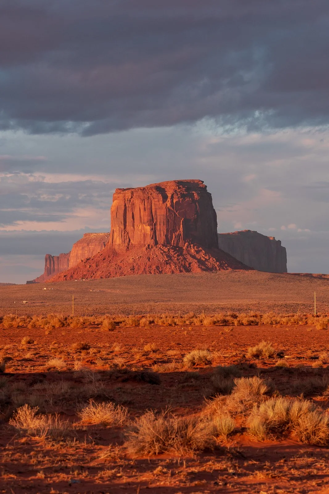 Paysage désertique avec de grandes formations rocheuses rouges, probablement dans le sud-ouest des États-Unis, avec un ciel nuageux à l'aube ou au crépuscule.