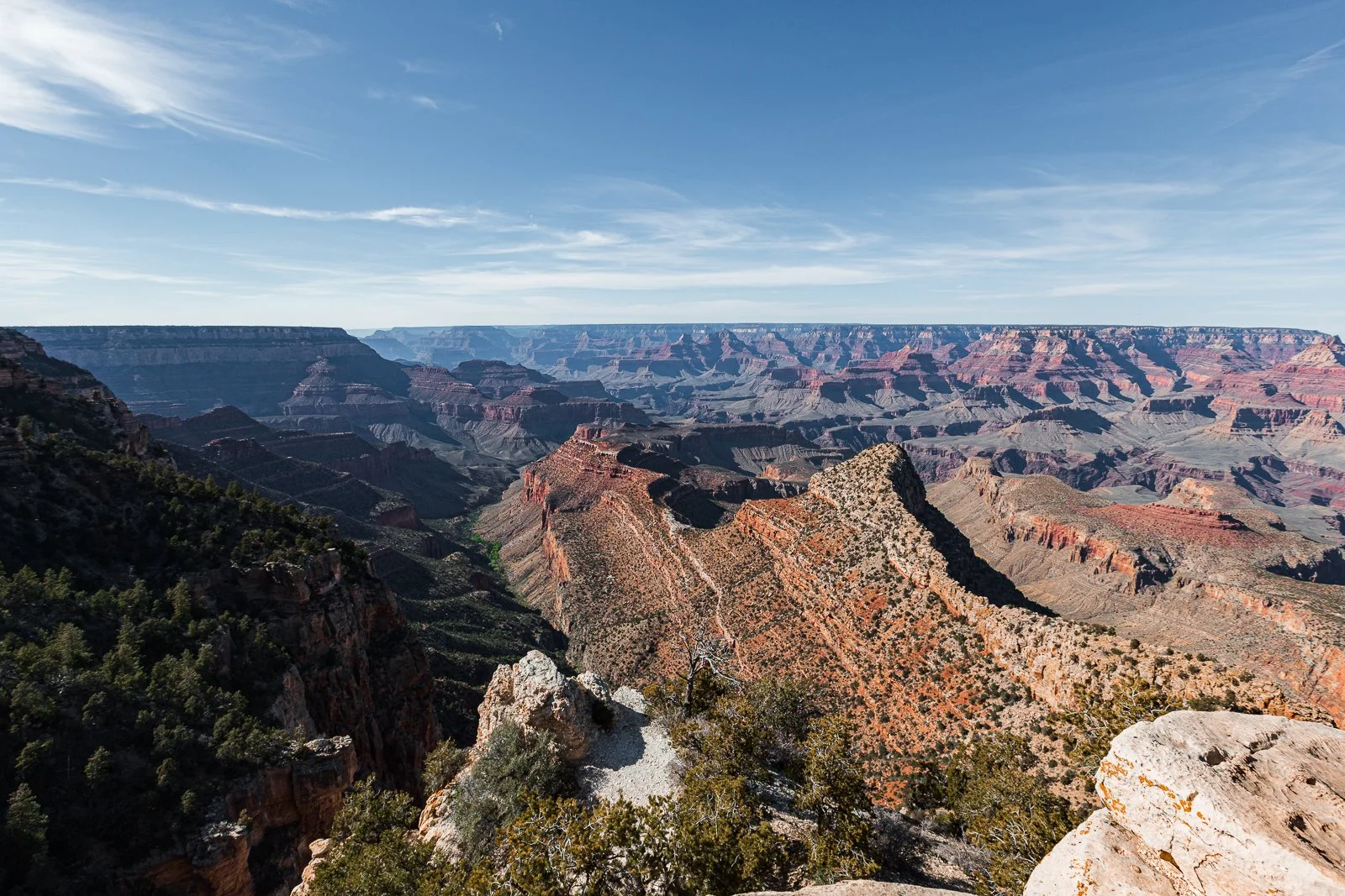 Vue panoramique du Grand Canyon avec ses formations rocheuses colorées et ses canyon profond sous un ciel clair et ensoleillé.