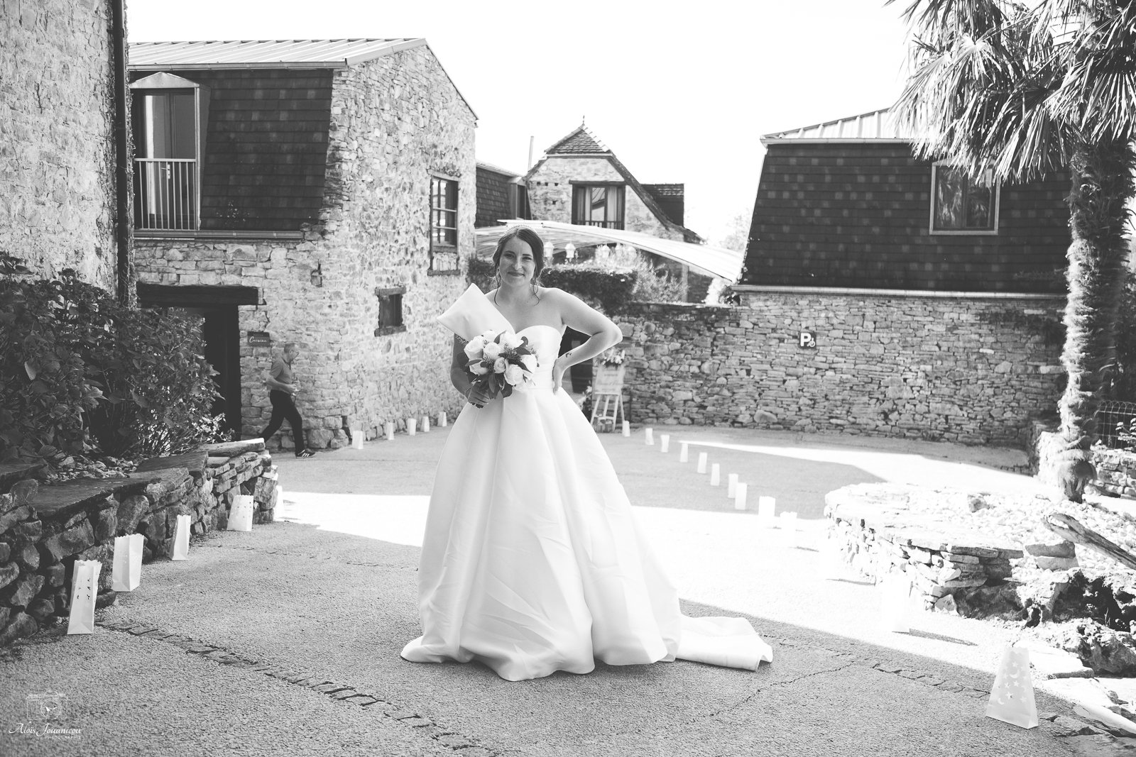 Une mariée en robe de mariage blanche posant avec un bouquet de fleurs devant un bâtiment en pierre