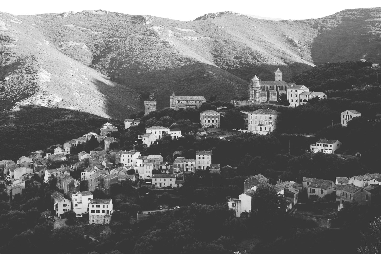 Un village perché dans une vallée montagneuse, avec des bâtiments en pierre et une église au centre, entouré de montagnes escarpées et de forêts.