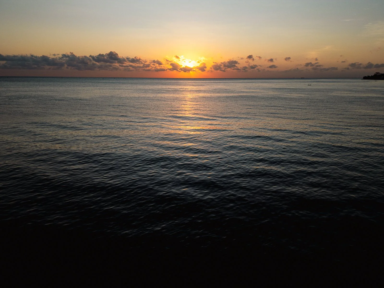 Coucher de soleil sur l'océan avec des nuages au loin et des eaux calmes.