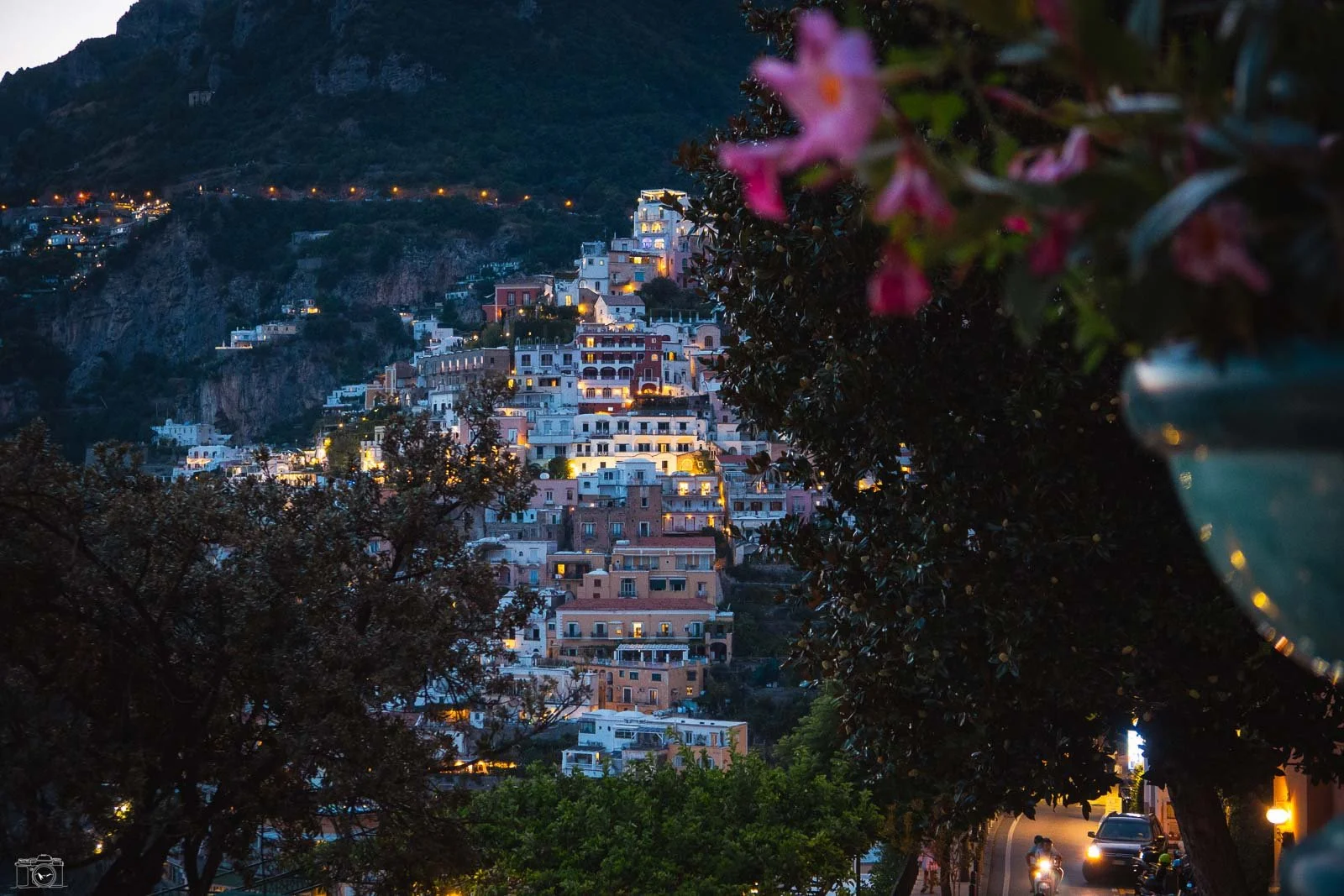 Vue de la ville de Positano sur la côte amalfitaine en Italie, prise au crépuscule, avec les maisons colorées illuminées sur la colline, entourée de montagnes et d'arbres.