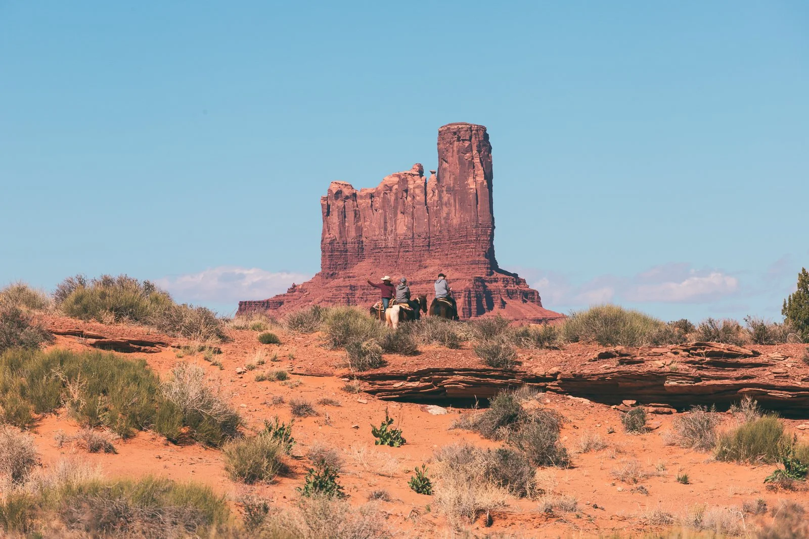 Trois personnes à cheval dans un désert proche d'une formation rocheuse emblématique, le monument Valley, au coucher du soleil.