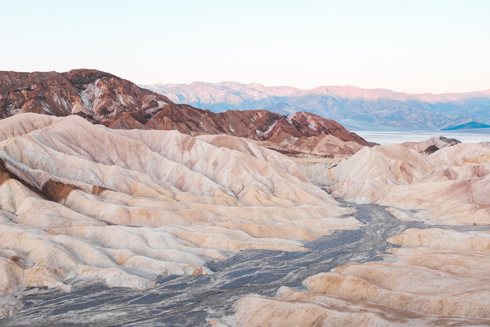 Paysage désertique avec montagnes aux couleurs variées, terrain rocheux et canyon au premier plan sous un ciel clair.