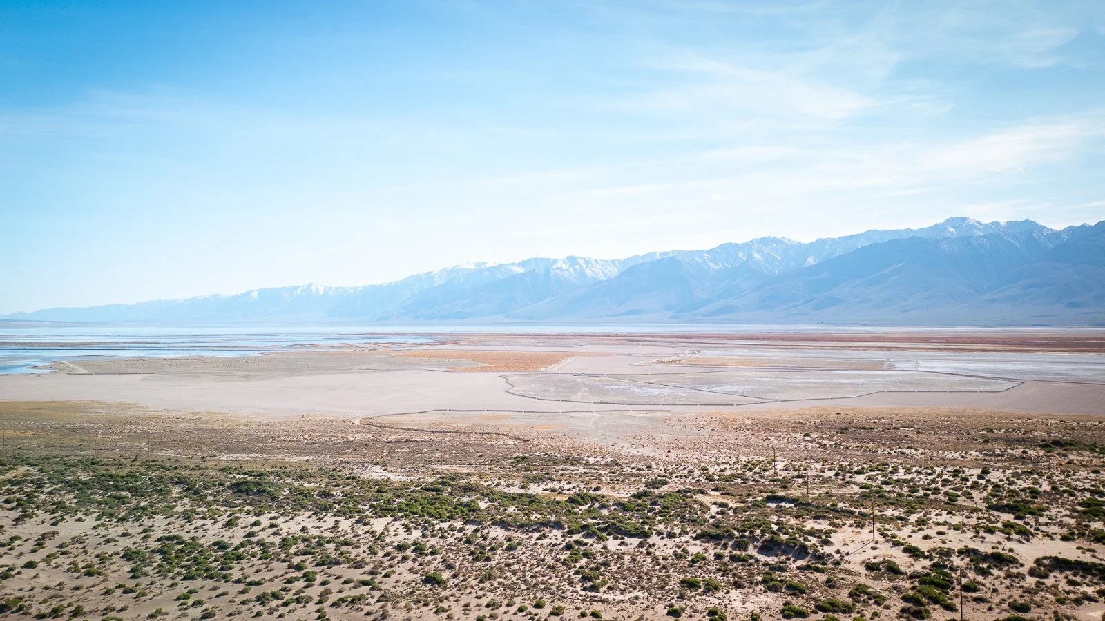 Paysage désertique avec montagnes enneigées au loin, zone saline ou lac asséché au centre, végétation sparse au premier plan.
