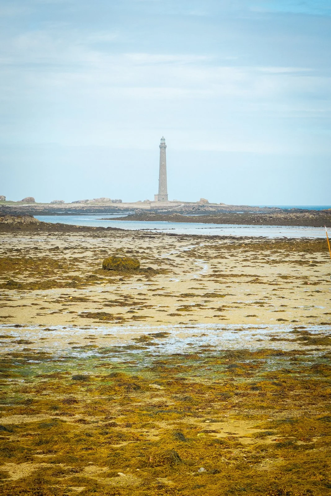 Phare en pierre sur une côte rocheuse vue de la plage, ciel nuageux.
