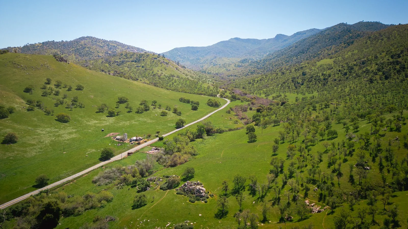 Paysage de montagnes verdoyantes avec une route sinueuse traversant la vallée et de petits bâtiments près de la route.
