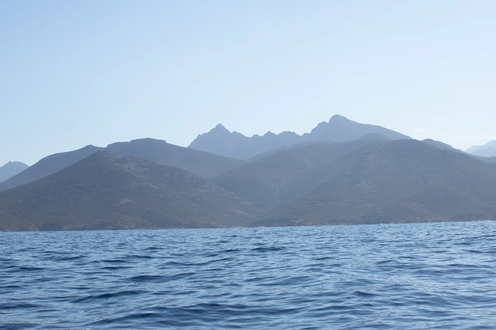 Paysage de montagne et mer avec vagues sous un ciel clair.