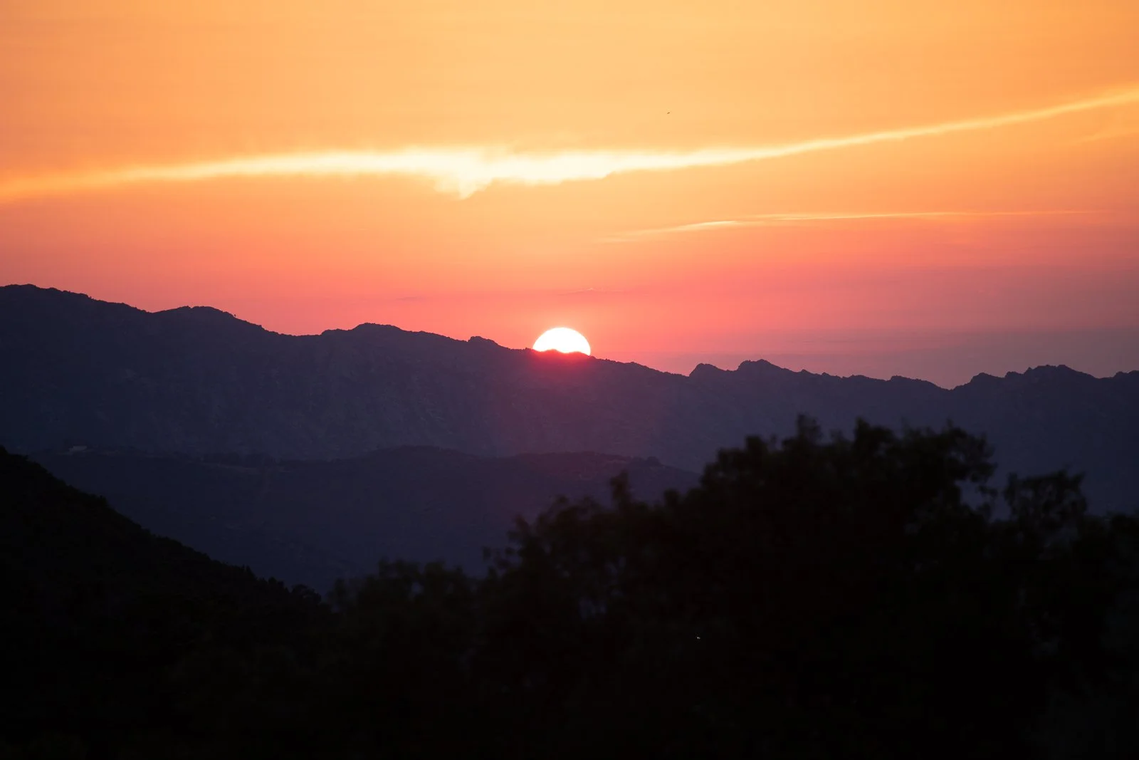 Coucher de soleil sur des montagnes avec ciel coloré en orange, rose et jaune, silhouette des montagnes en premier plan.