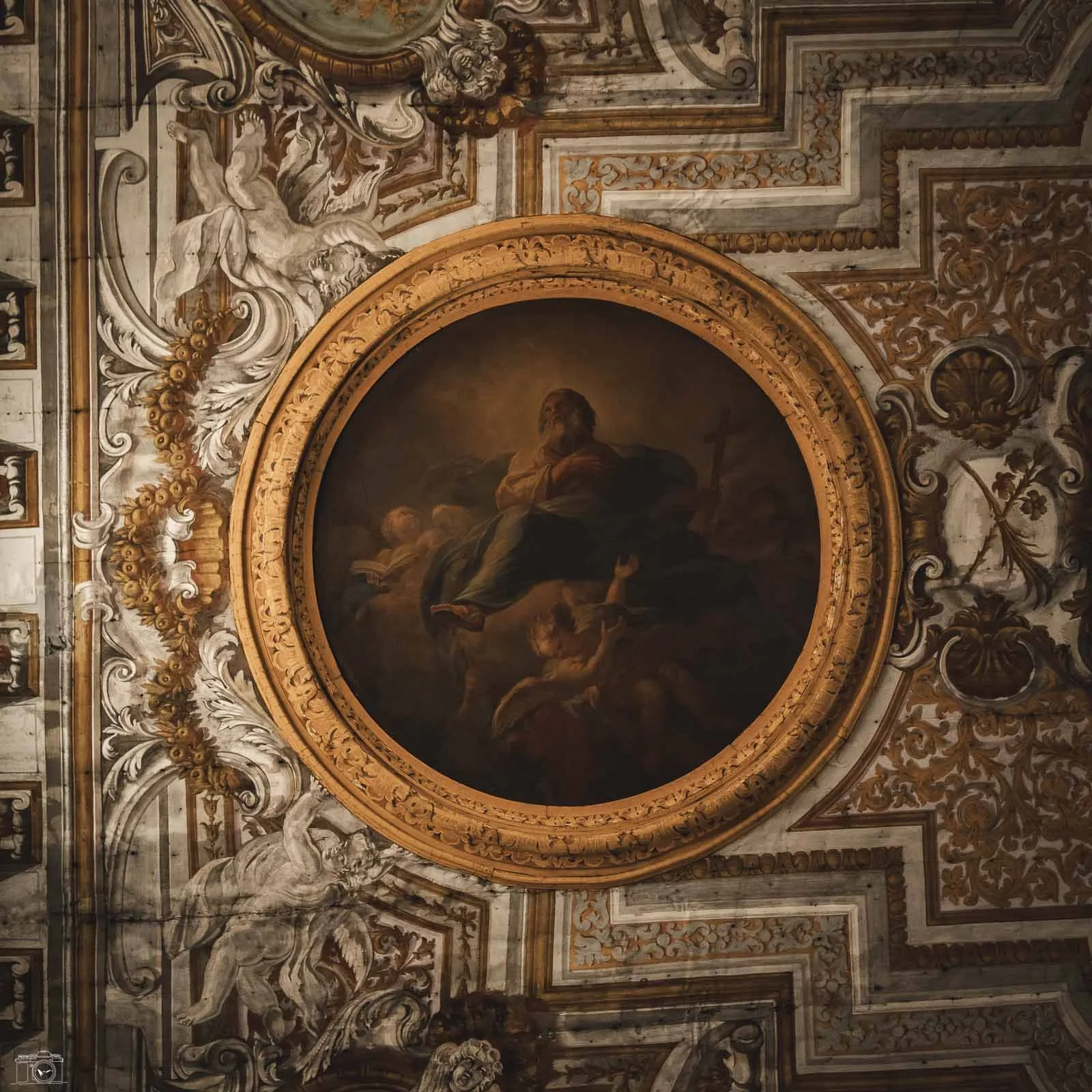 Détail d'une fresque de plafond représentant un portrait religieux entouré de décorations baroques ornées de motifs dorés et blancs.