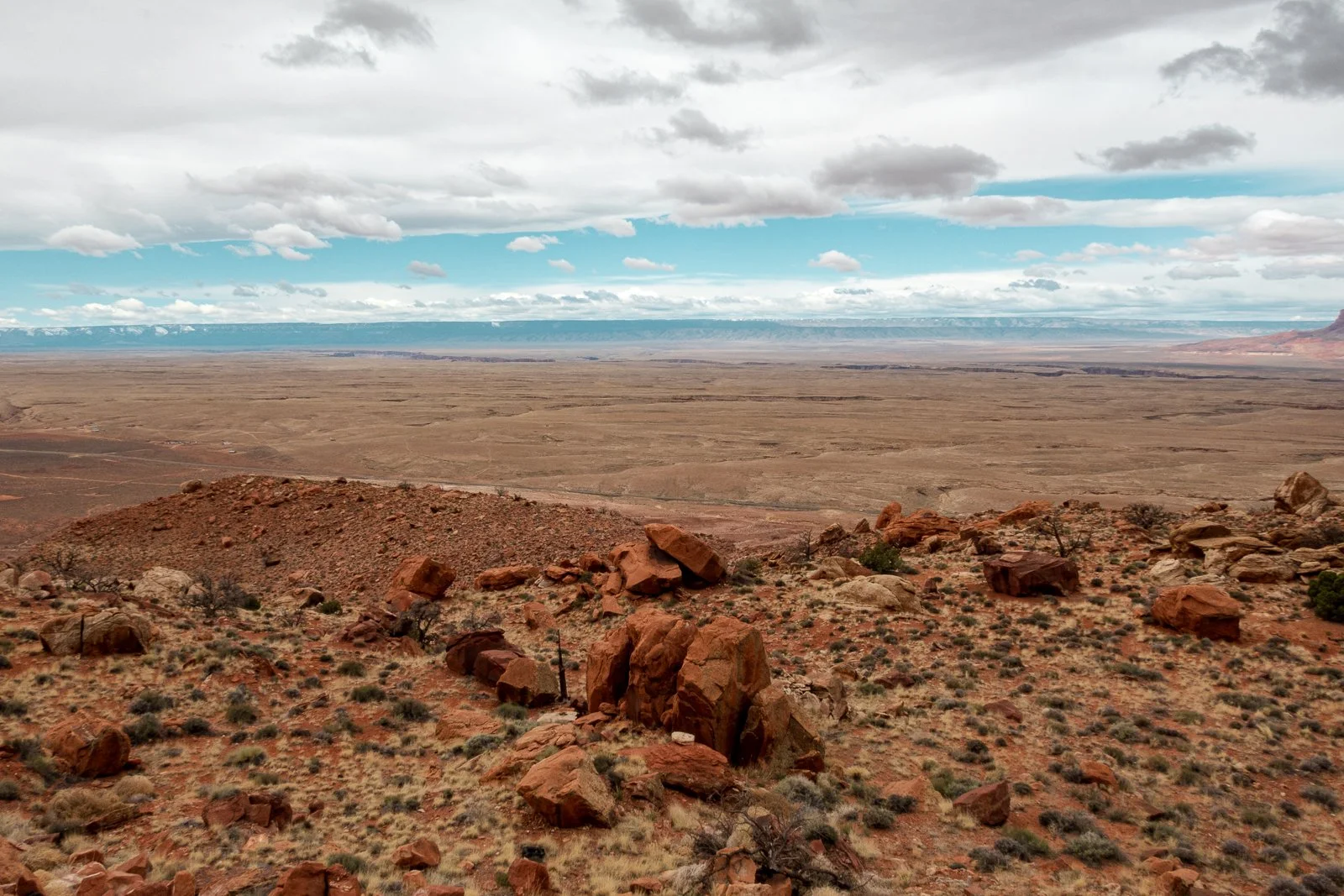 Paysage désertique avec roche rouge et terrain aride, sous un ciel nuageux.