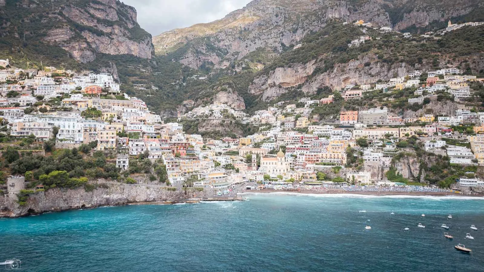 Vue de la côte avec des maisons colorées construite sur une paroi rocheuse et une mer turquoise au premier plan, avec quelques bateaux.