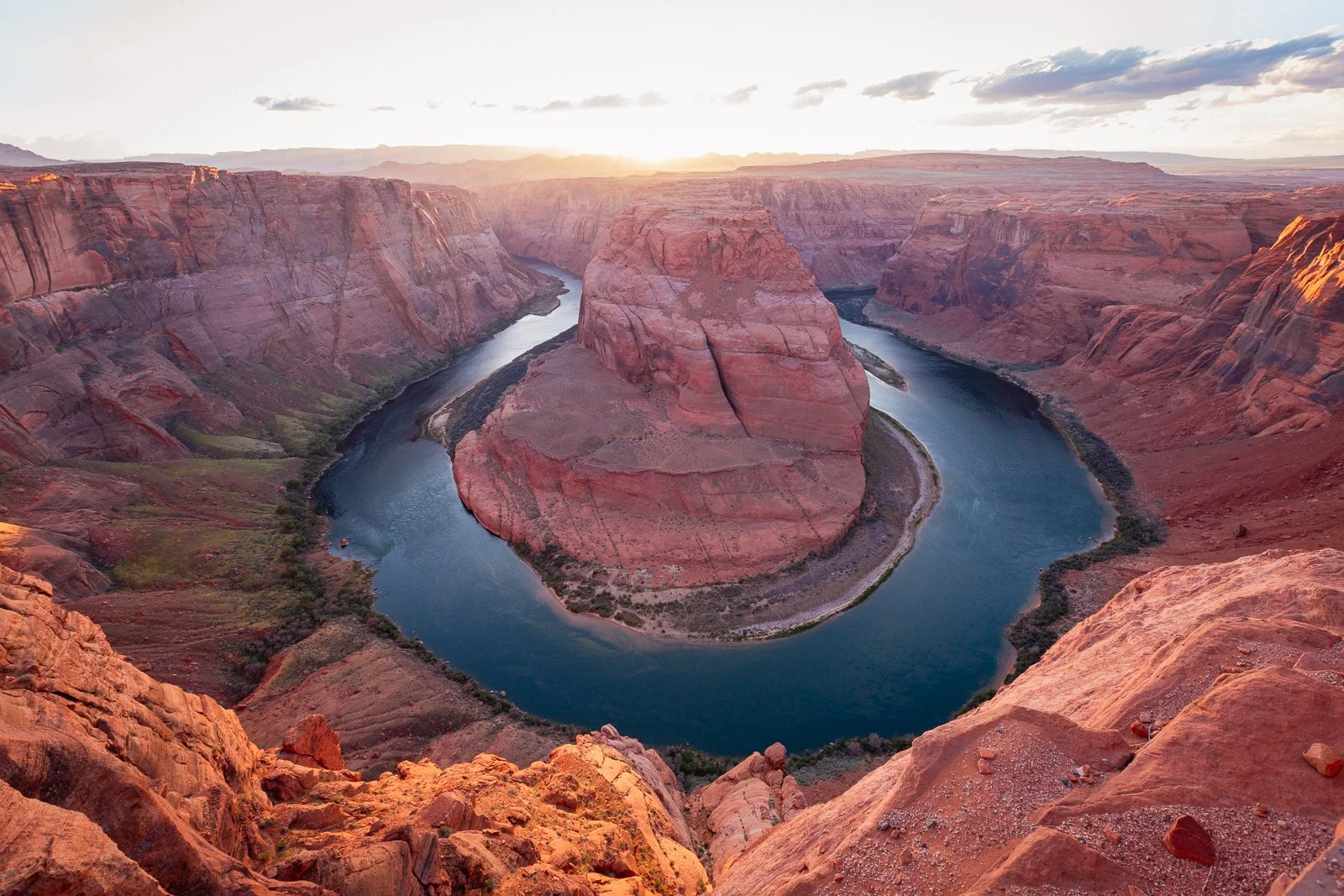 Vue panoramique du canal de Colorado avec un rocher au centre, entouré de hautes falaises rocheuses rouges au coucher du soleil.