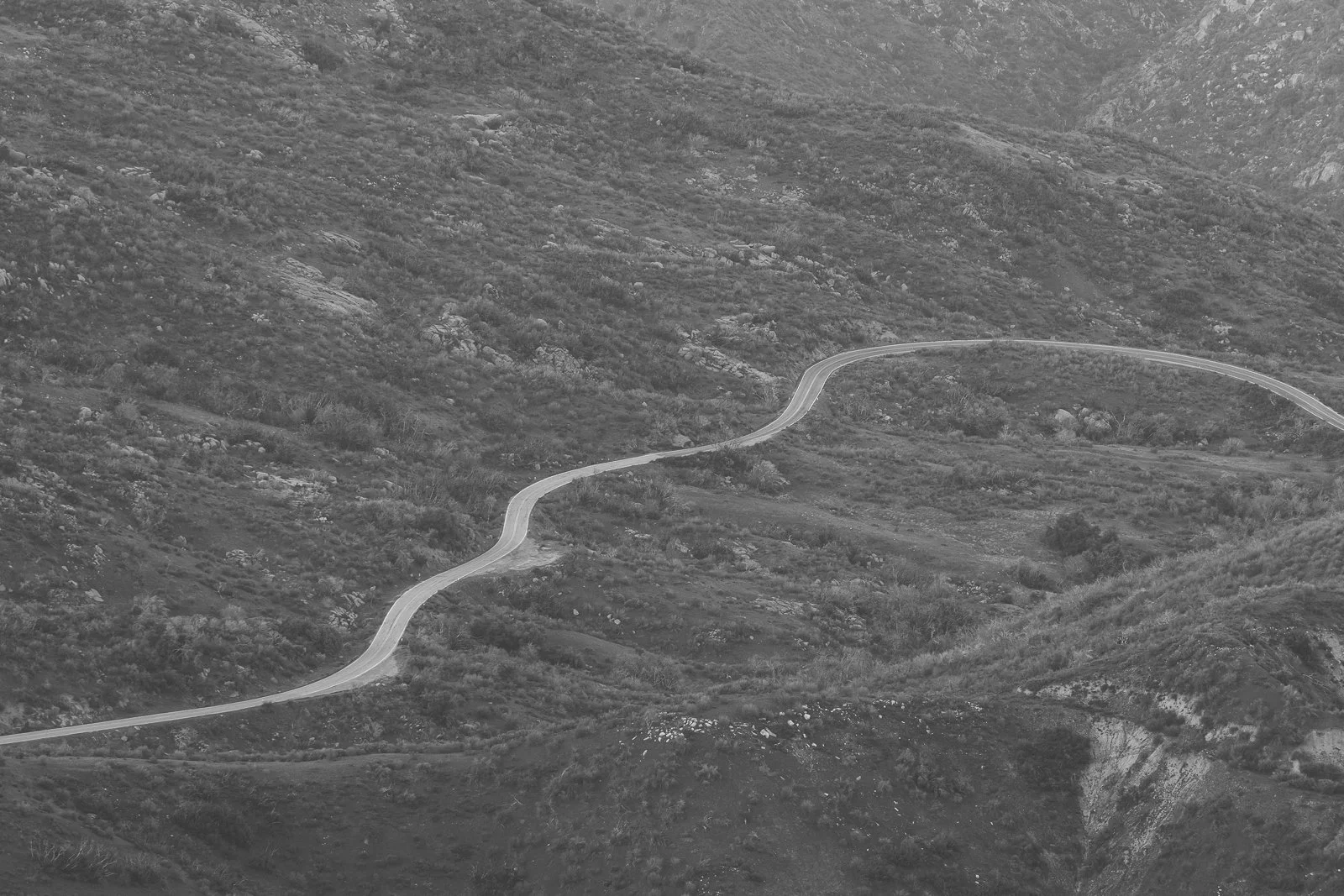 Une route sinueuse traverse une région montagneuse. La scène est en noir et blanc.