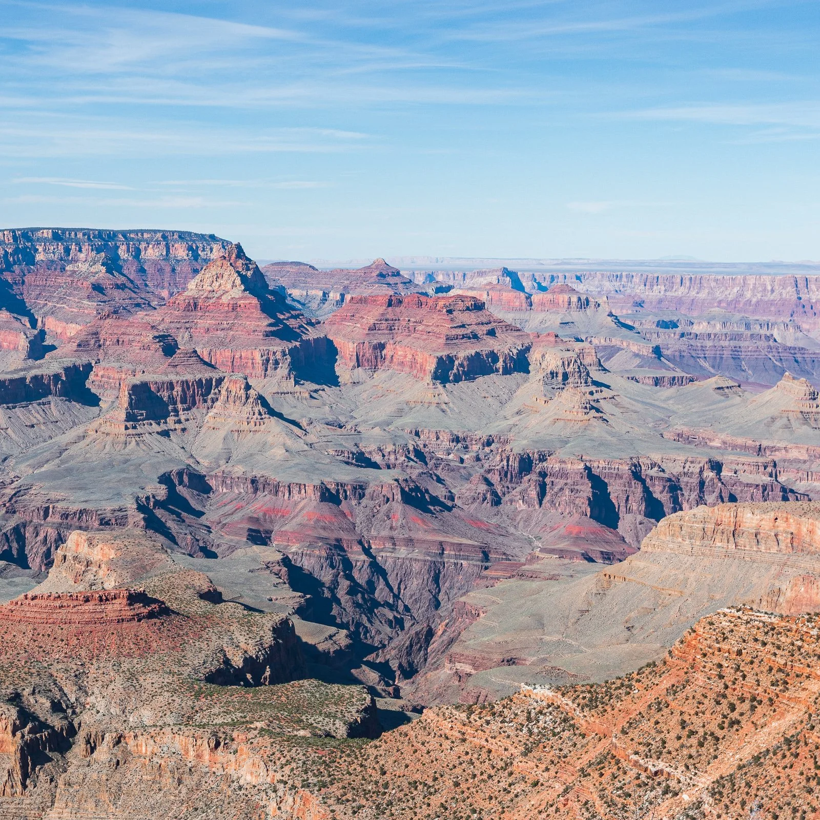 Vue panoramique du Grand Canyon au coucher du soleil, montrant ses strates multicolores et ses formations rocheuses érodées.