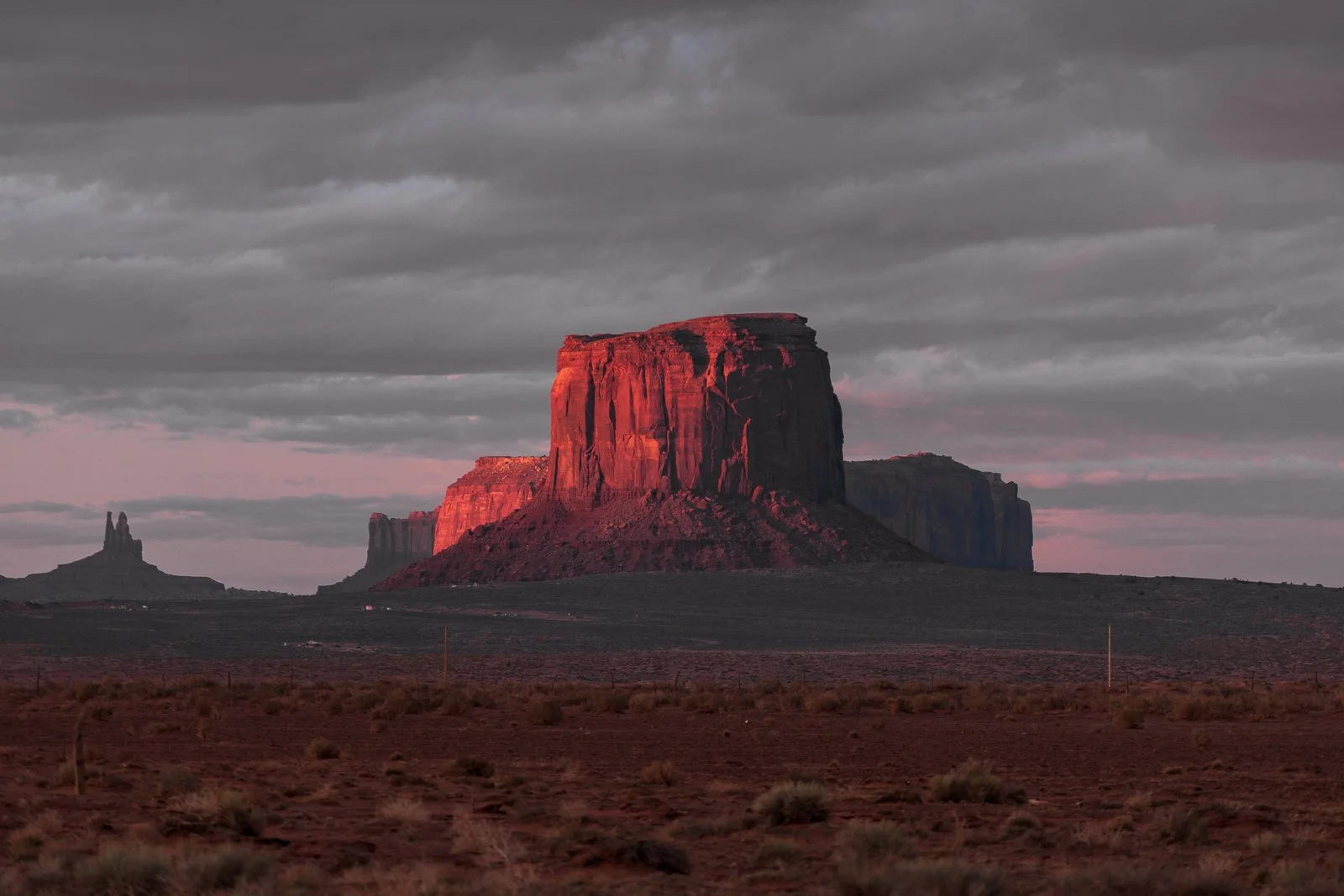 Un paysage désertique avec un grand monument rocheux rouge, typique du parc national de Monument Valley dans l'Arizona, sous un ciel nuageux. 