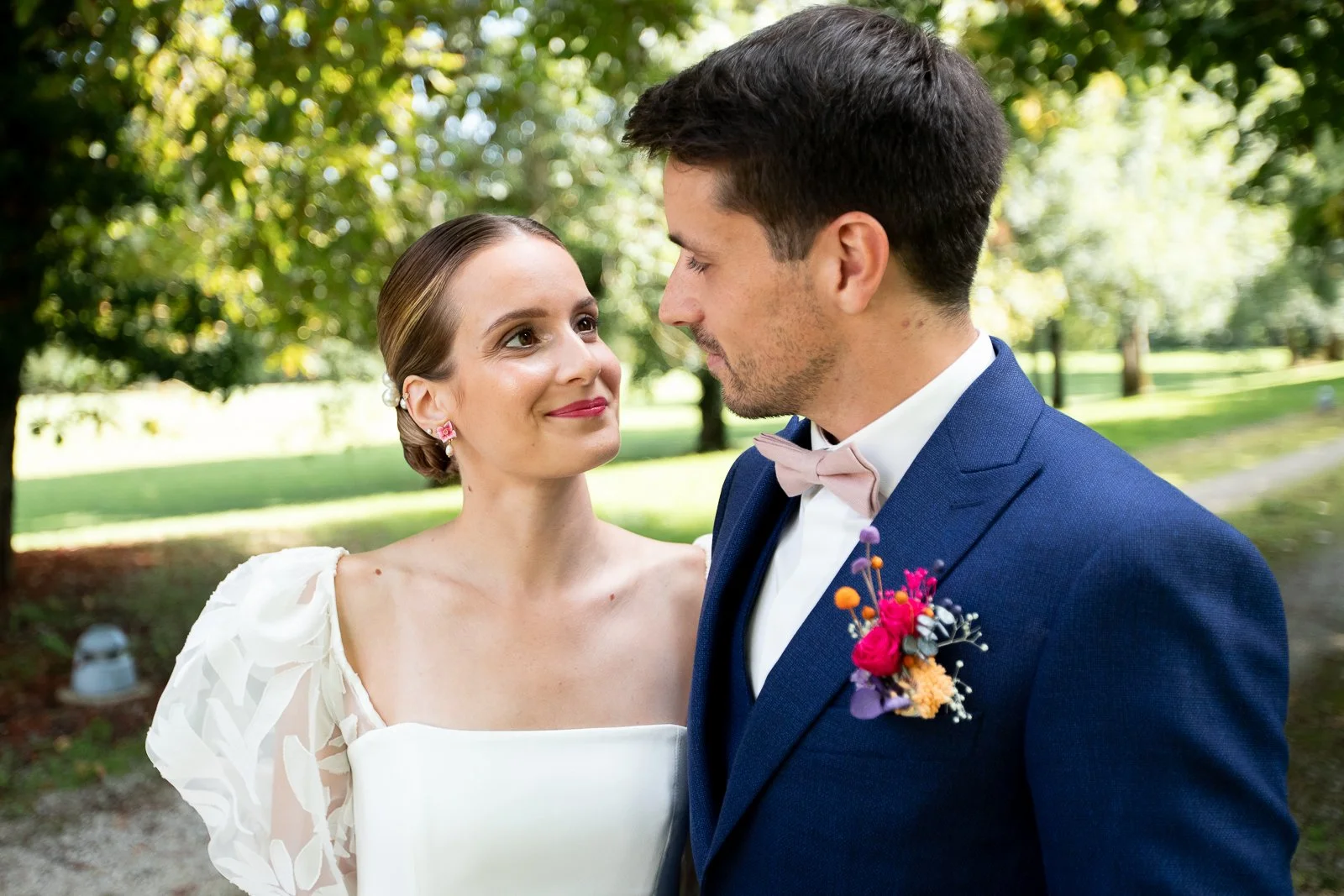 Un couple en vêtements de mariage regarde affectueusement dans les yeux lors d'une cérémonie en plein air dans un parc verdoyant.