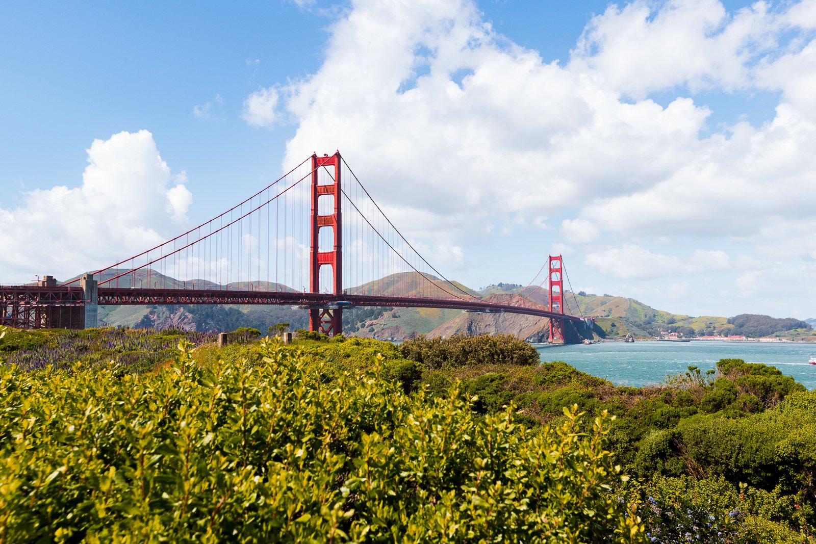 Le pont du Golden Gate sur l'océan avec des collines verdoyantes et un ciel bleu avec des nuages.