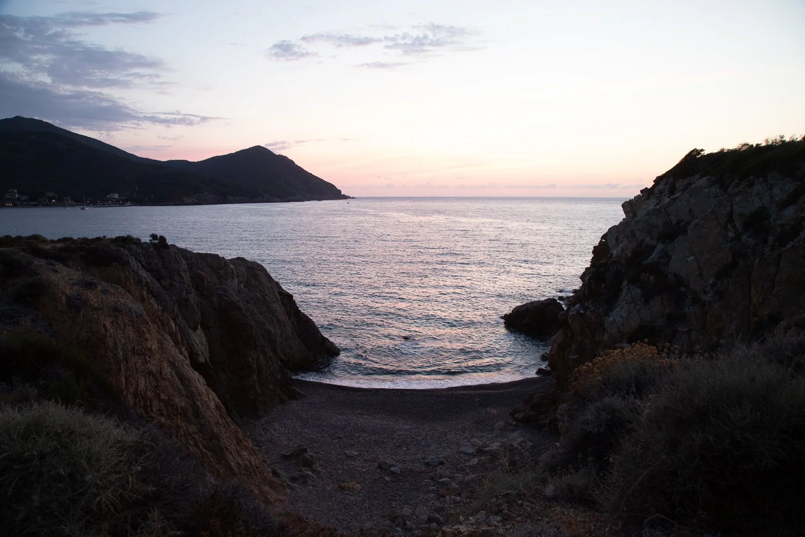 Coucher de soleil sur une baie rocheuse avec des collines en arrière-plan.