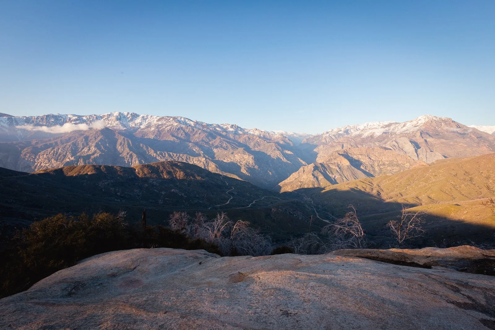 Paysage de montagnes avec sommets enneigés, vallée et chemins serpentant à travers les collines, ciel clair