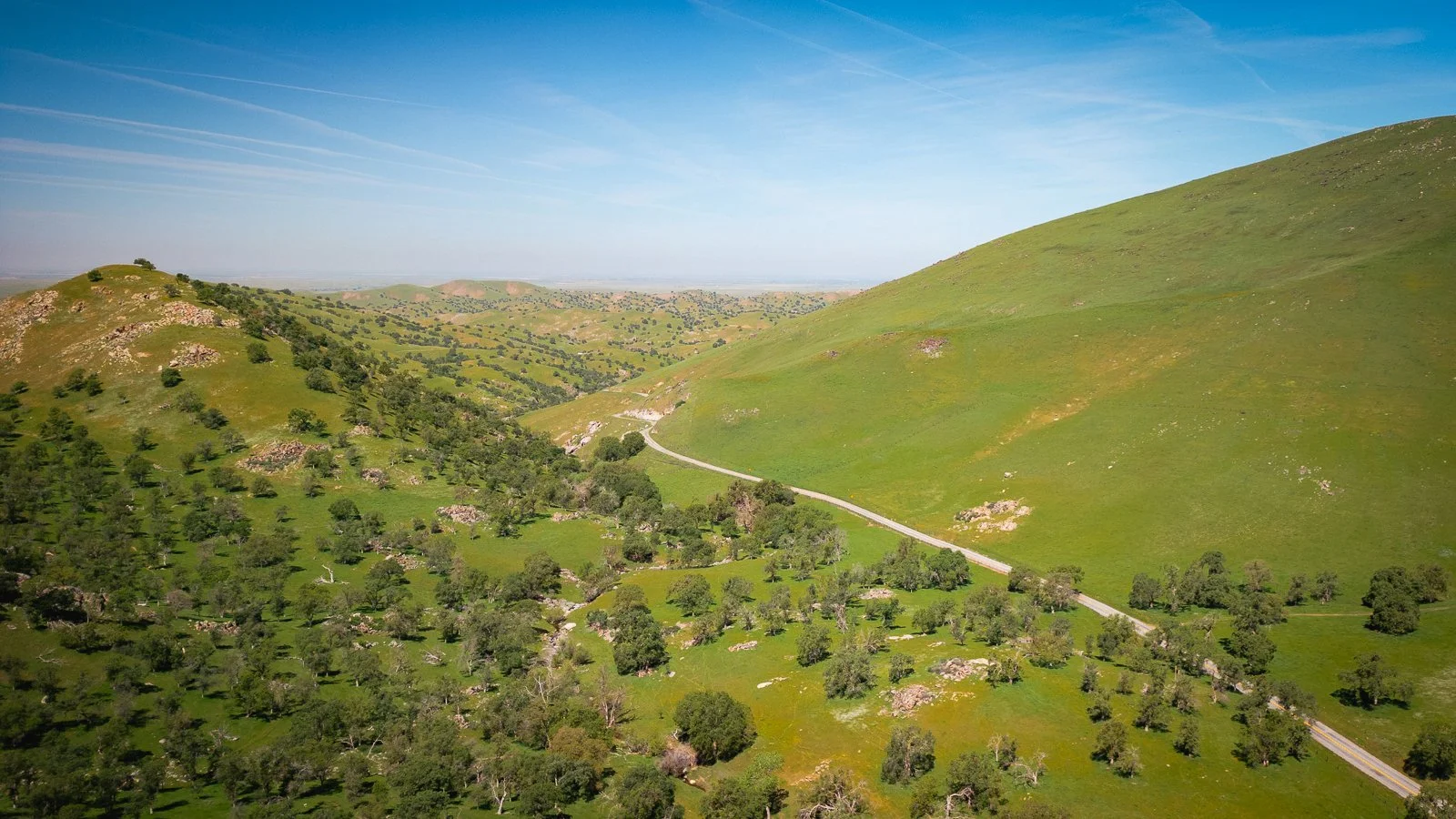 Paysage de collines verdoyantes avec une route serpentant à travers la vallée sous un ciel bleu clair.
