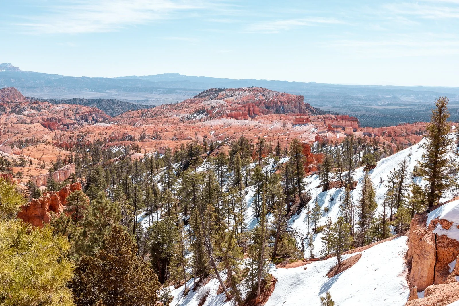 Paysage de canyon avec arbres et montagnes rocheuses, neige sur le sol, ciel en partie dégagé.